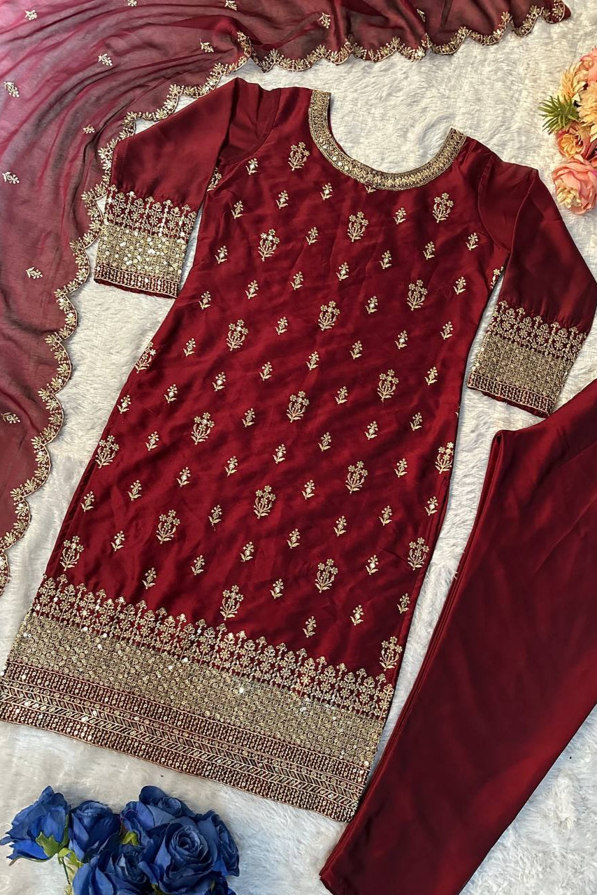 Maroon embroidered traditional outfit with gold details on a textured surface with flowers.