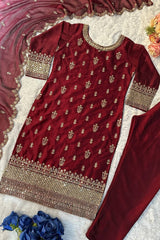 Maroon embroidered traditional outfit with gold details on a textured surface with flowers.